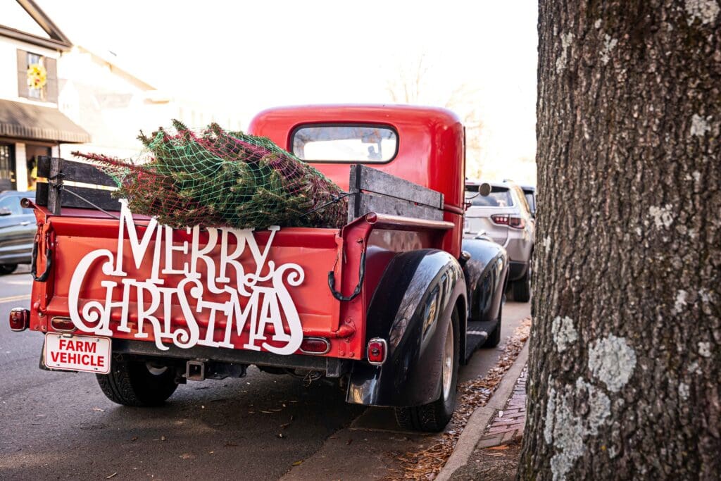 Red truck hauling a Christmas tree with a "Merry Christmas" sign on the bumper